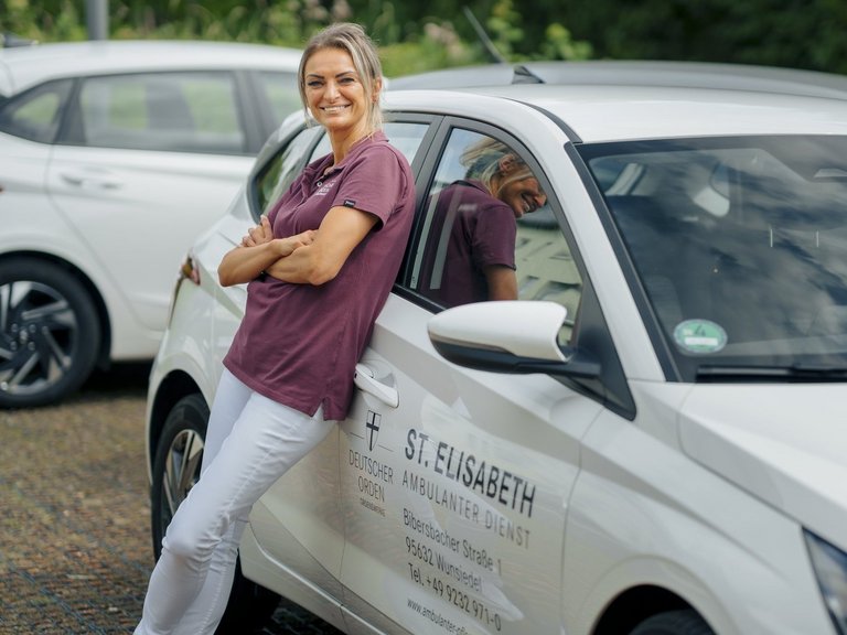 Eine junge Pflegerin in ihrem Auto mit der Aufschrift: "St. Elisabeth Ambulante Pflege - Heilen und Helfen"