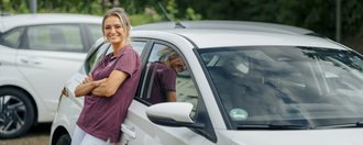 Eine junge Pflegerin in ihrem Auto mit der Aufschrift: "St. Elisabeth Ambulante Pflege - Heilen und Helfen"