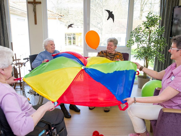 vier Frauen "balancieren" einen Luftballon mit Hilfe eines großen Tuchs, das sie gemeinsam halten