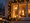 Ein festlich erleuchtetes Fenster bei Dämmerung, umrahmt von einer Tannengirlande mit Lichterketten. Im Inneren hängen eine leuchtende Stern-Dekoration und eine große, beleuchtete Zahl Eins. Schnee liegt auf dem Fensterbrett und den Büschen im Vordergrund.